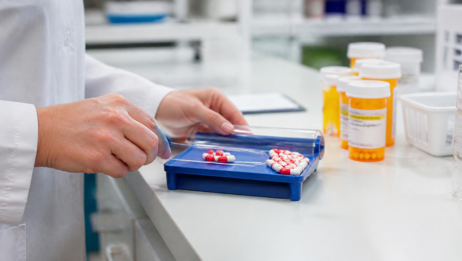 Pharmacist counting capsules on a pill tray beside prescription bottles